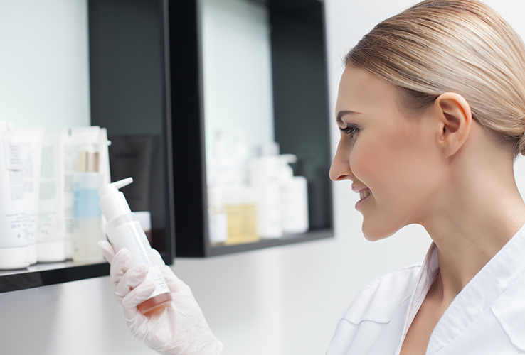 woman holding bottle in front of a shelf of various bottles of liquid